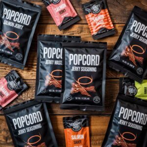 Assorted Popcord jerky seasoning and salmon jerky pouches arranged on a wooden table, showcasing bold black flexible packaging with high-impact graphics.